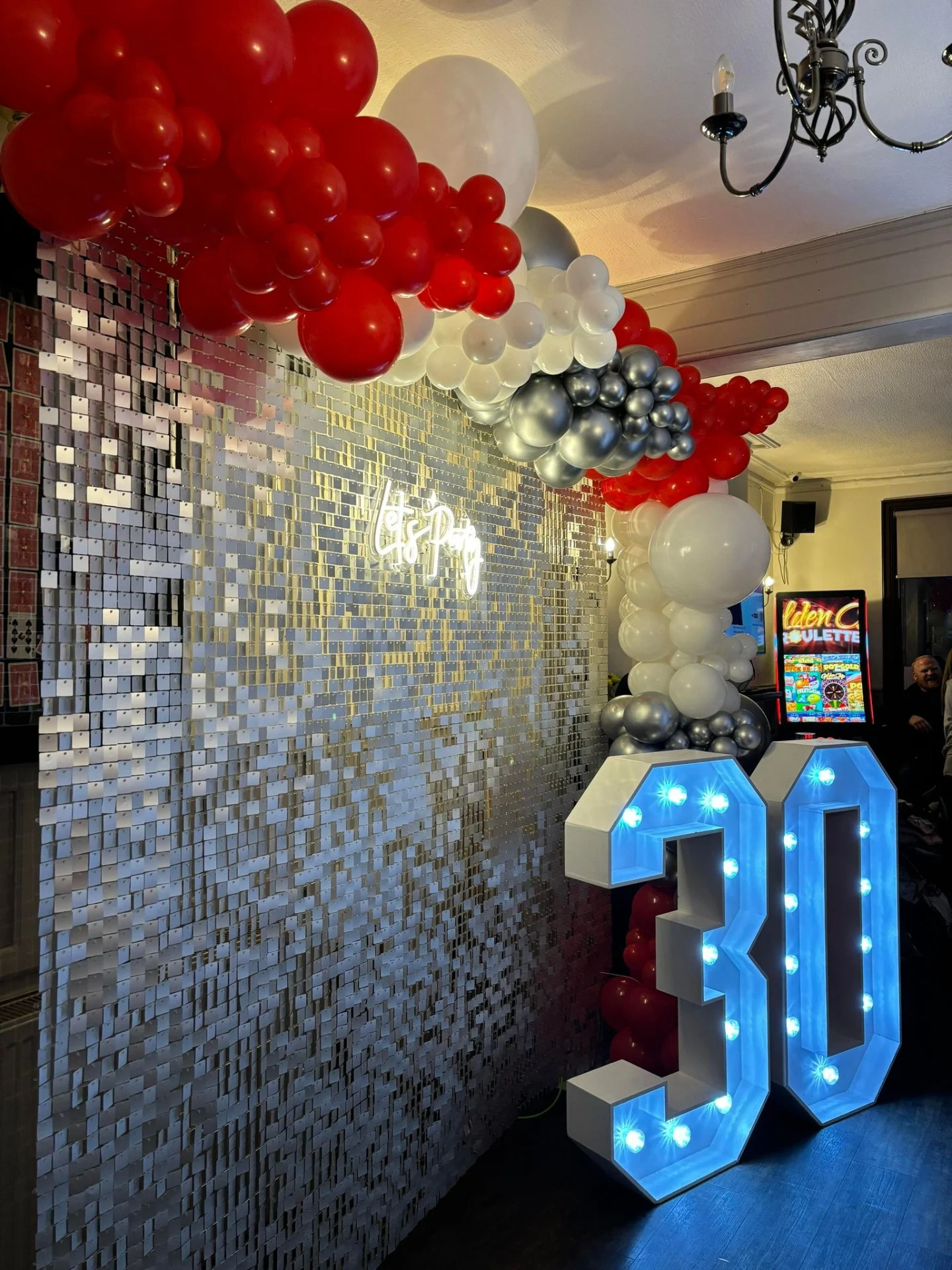 Silver shimmer wall hire with balloon and LED number decorations