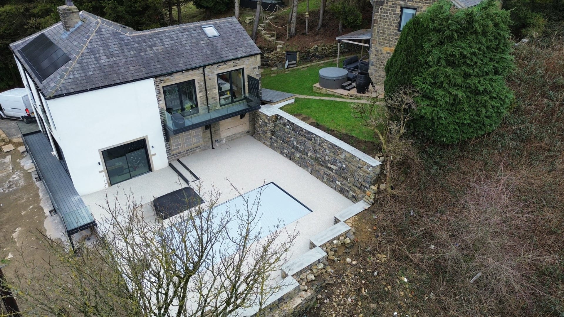 Aerial view of a modern house with a landscaped courtyard, stone retaining walls, and outdoor patio and swimming pool 