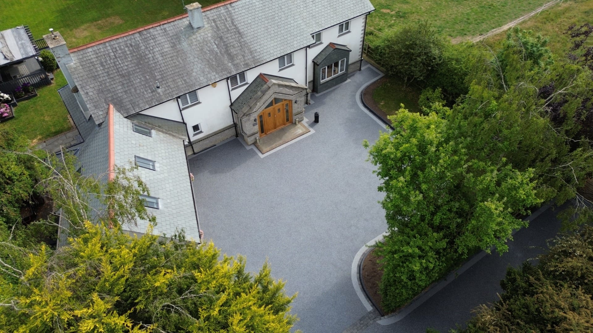 Aerial view of a traditional countryside house with a large Resin Bound driveway in Essex surrounded by trees and gardens.