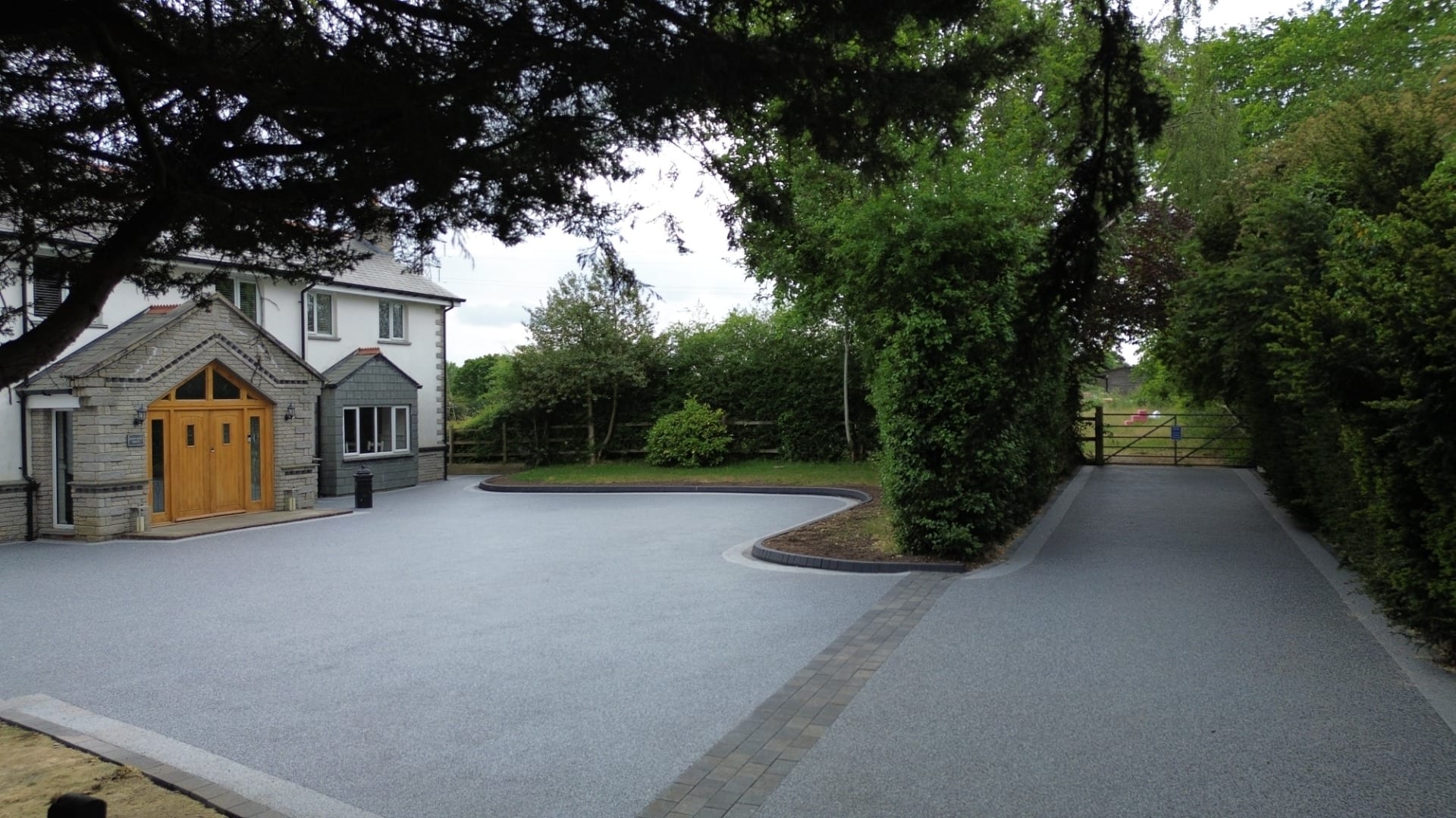 Resin-bound driveway outside a countryside house with landscaped edges and gated entrance.