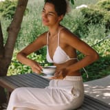 Modelo tomando tereré en un patio con el corpiño Yvoty blanco y pantalón de lino