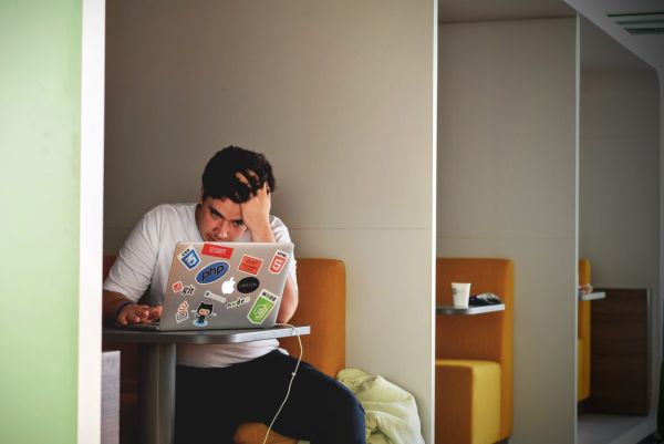 A man holds his head in his hand in frustration while looking at his laptop