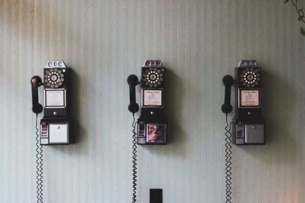 Three vintage rotary payphones hanging on a wall