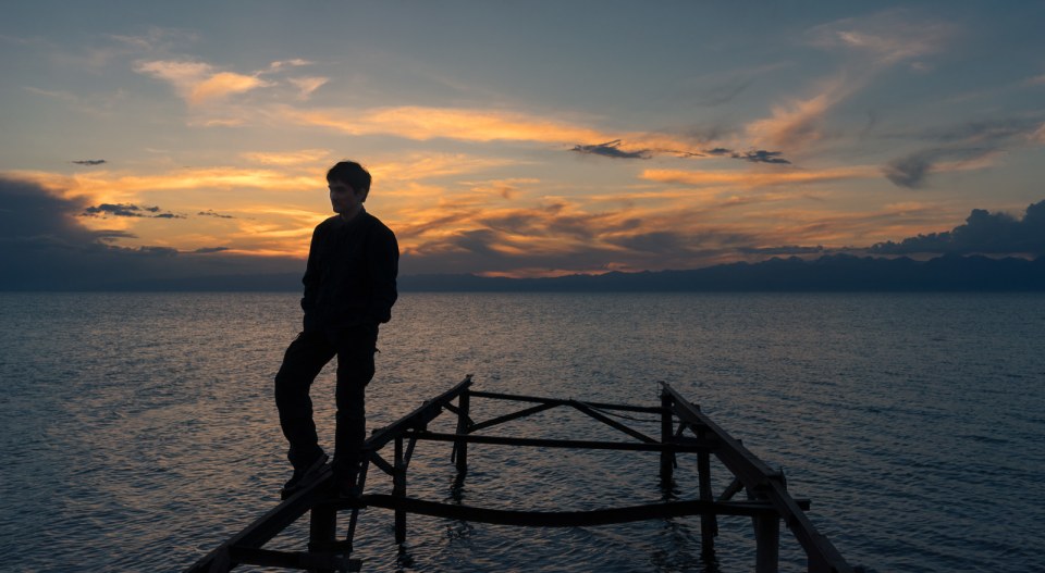 Man standing on the metal frame of an abandoned dock on Issyk-Kul lake at dusk in Issyk-Kul region, Kyrgyzstan.