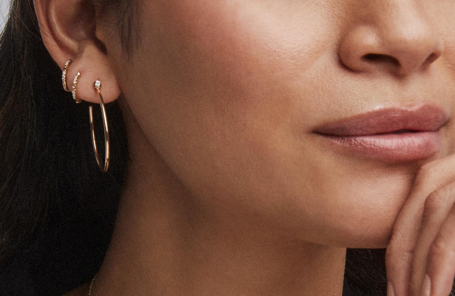 Close up of model wearing one hoop and two huggie earrings.