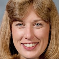 Headshot of astronaut Jan Davis in blue flight suit holding a model space shuttle in front of the U.S. flag
