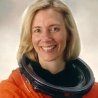 Astronaut Susan Kilrain in orange space suit without helmet, crossing arms and smiling