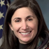 Headshot of astronaut Nicole Stott in orange space suit without helmet in front of the U.S. flag