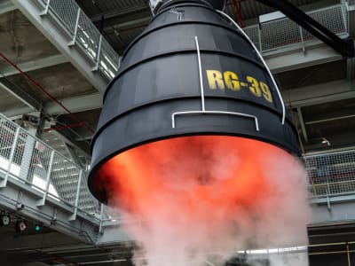 A billow of steam escapes from the nozzle of a hanging engine. Red light glows inside the nozzle, and the word "RG-39" is painted on in yellow across the black nozzle.