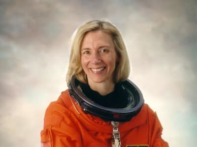 Astronaut Susan Kilrain in orange space suit without helmet, crossing arms and smiling