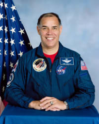 Tête de l'astronaute Fred Gregory en combinaison de vol bleue devant le drapeau américain.