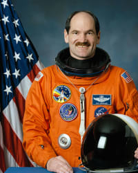 Tête de l'astronaute Guy Gardner en combinaison de vol orange, casque en main.