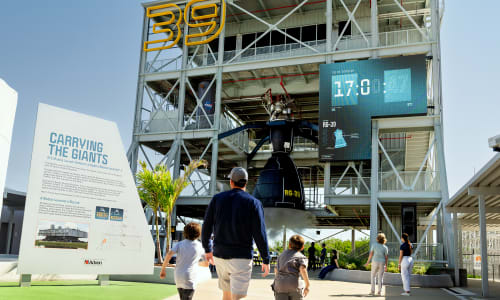 The test fire rocket engine mounted from the third floor of the gantry. When the show countdown reaches zero, it comes to life in a roar of light, sound, mist, and static vibration. Nearby, an animation test loops on outward-facing monitors.