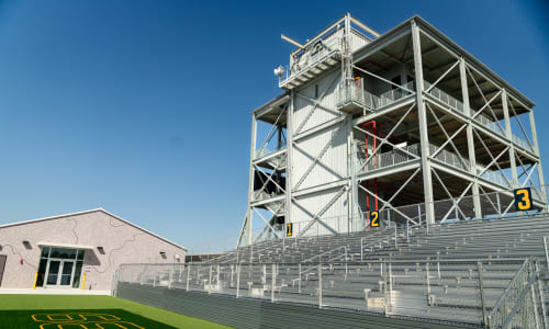 White bleachers stand in front of a four-story structure. The number 39 is painted onto the grass in front of the bleachers.