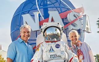 Husband and wife posing with an astronaut in front of the NASA fixture
