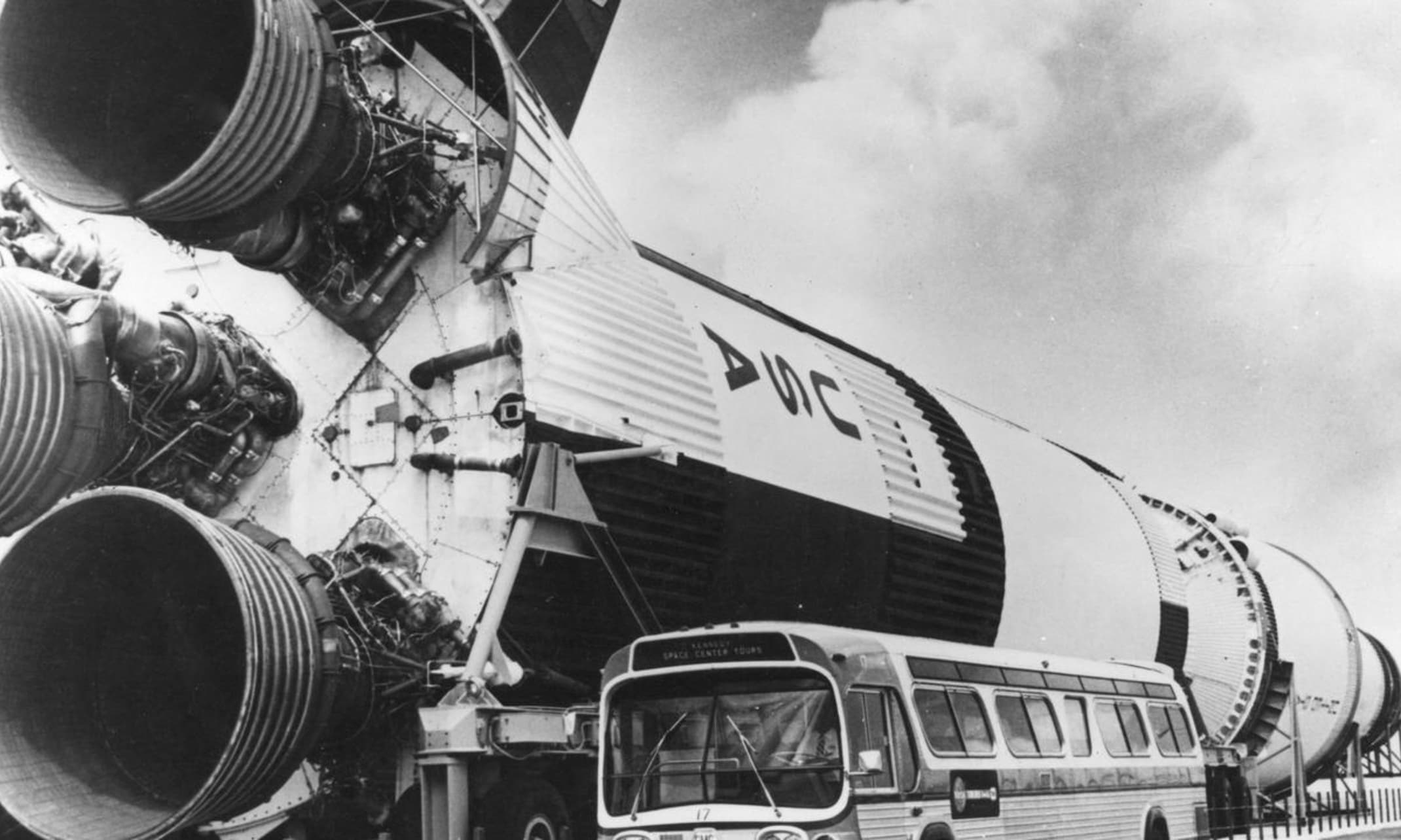 A bus parked outside the original outdoor display of the Saturn V Moon rocket. It was placed on its side outside near the Vehicle Assembly Building (VAB) beginning in the summer of 1976 as part of the U.S. Bicentennial Exposition on Science and Technology.