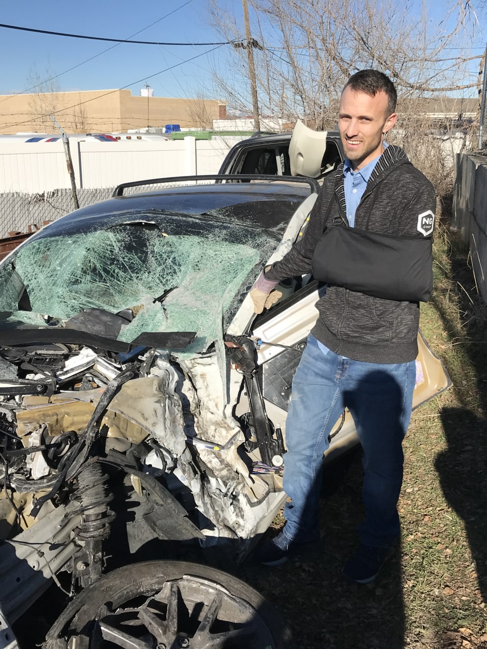 Kent standing by a wrecked Tesla model 3 in a junkyard. It's completely crushed.