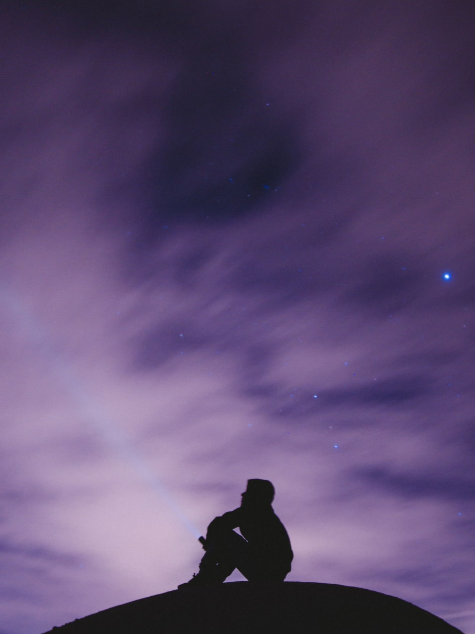 person sitting on black surface looking to a purple sky