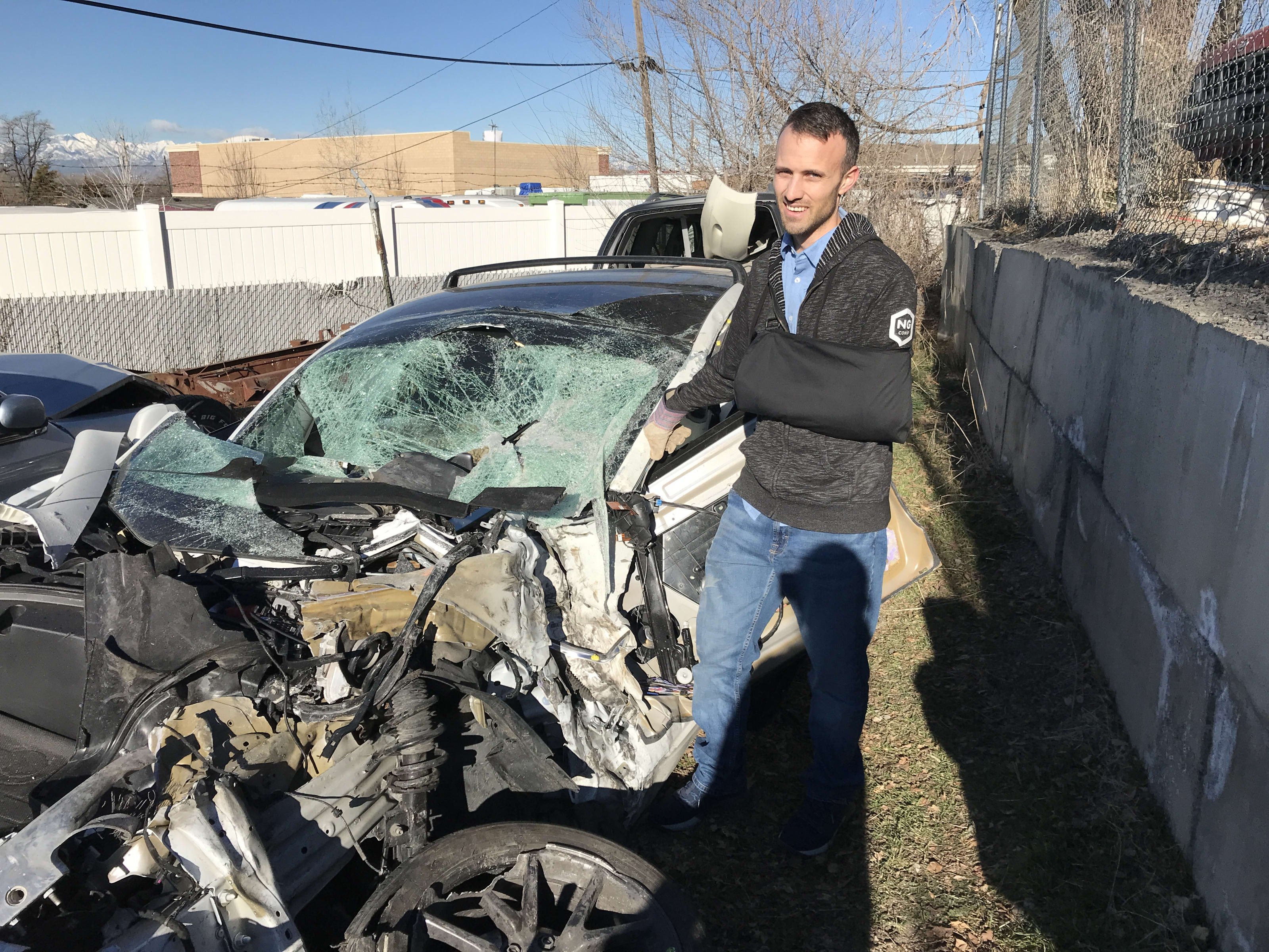 Kent standing by a wrecked Tesla model 3 in a junkyard. It's completely crushed.