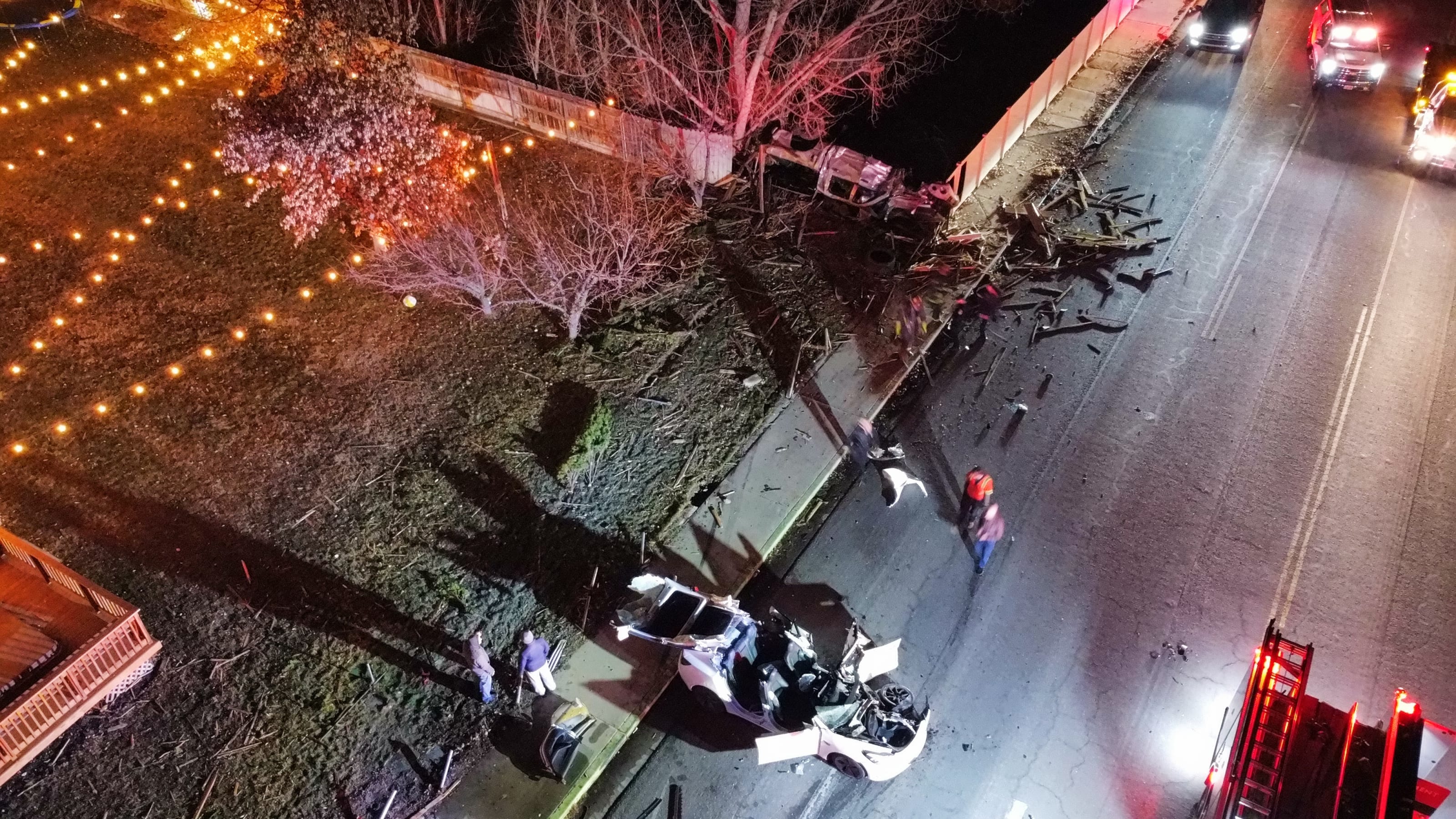 Night-time ariel view of a car accident showing a truck that had gone through the entire length of a fence. Debris is everywhere