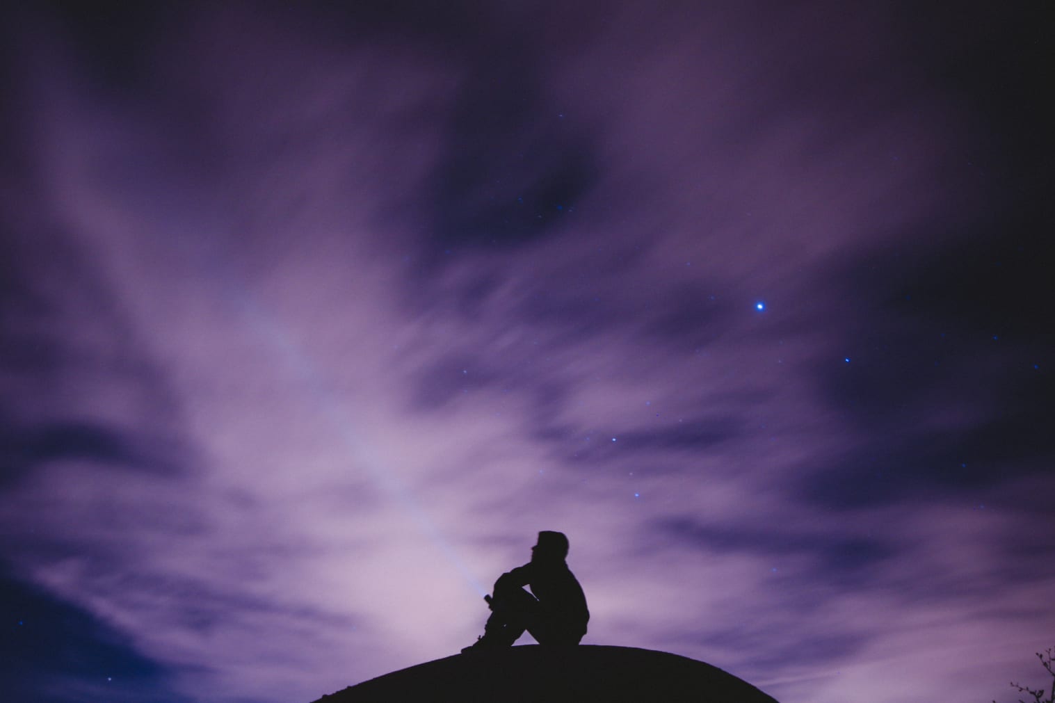 person sitting on black surface looking to a purple sky