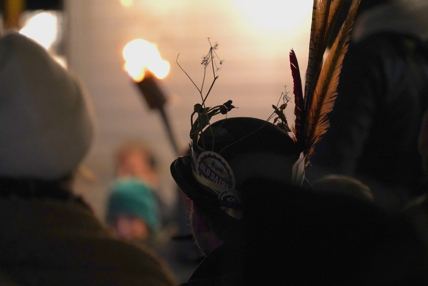 Person wearing hat adorned with pheasant feathers beer mats and foliage.