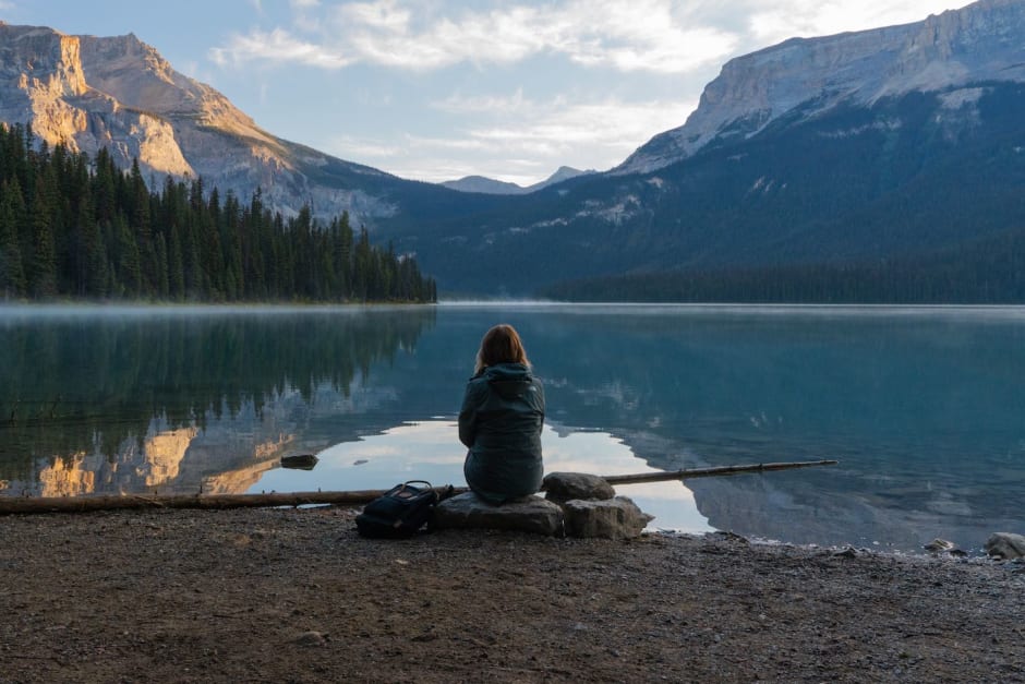 Harriet sat on a rock in front of Emerald Lake, Yoho National Park, with morning mist covering the surface of the water.