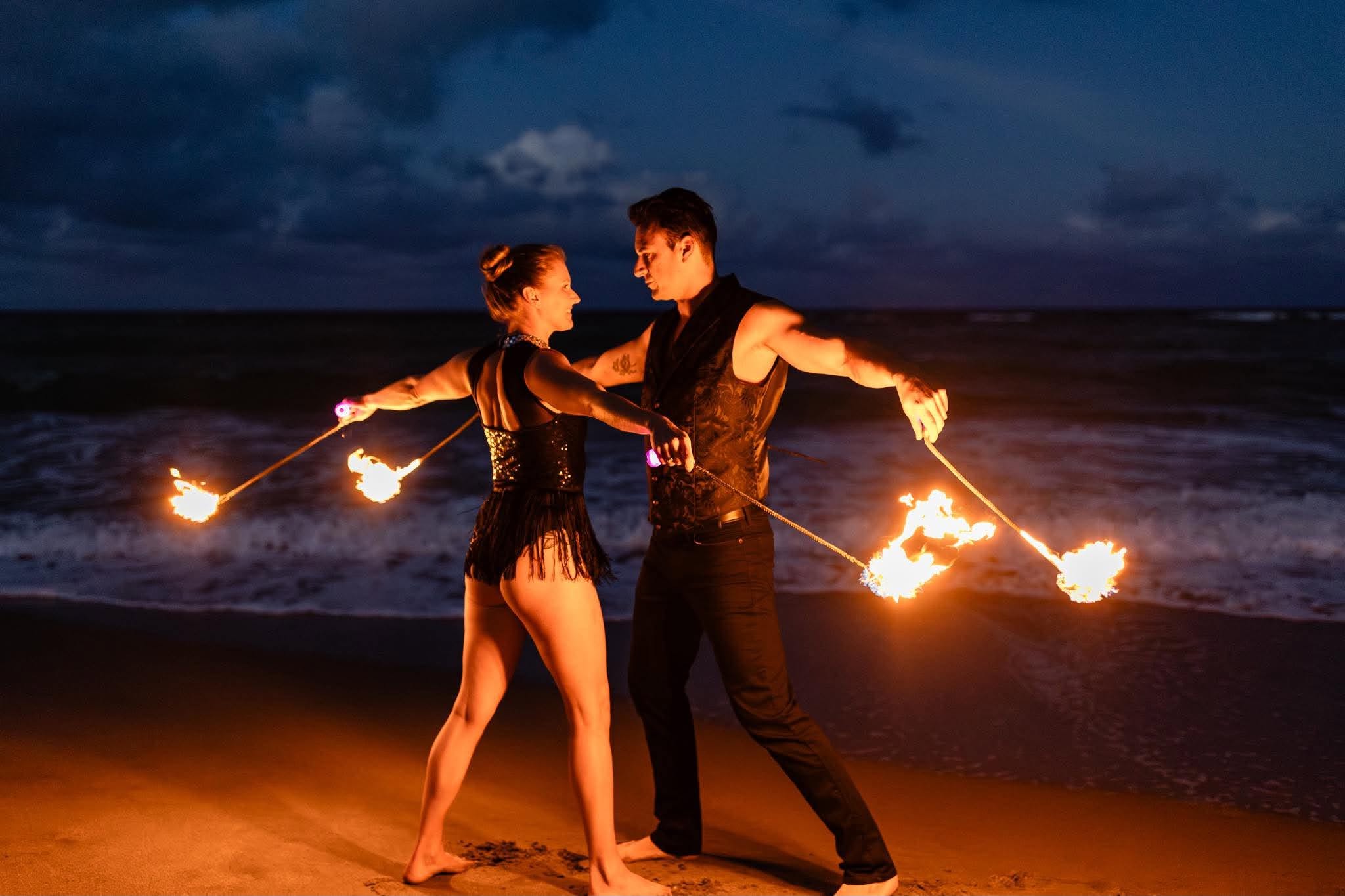 A flow artist performing with fire poi at night, glowing trails of orange light against a dark sky