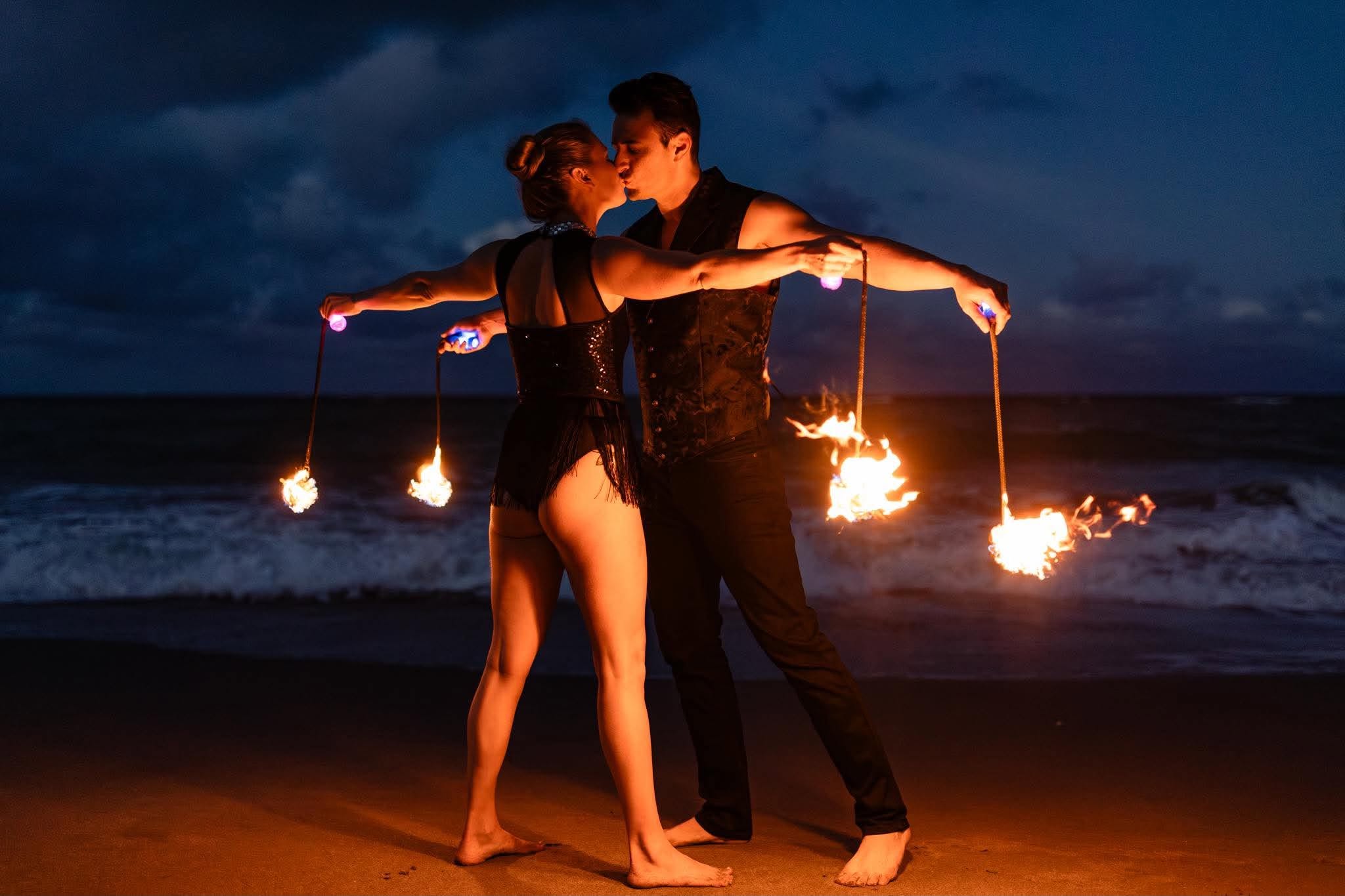Crystal and Robin moving together with fire props, illuminated trails of warm light against the darkness