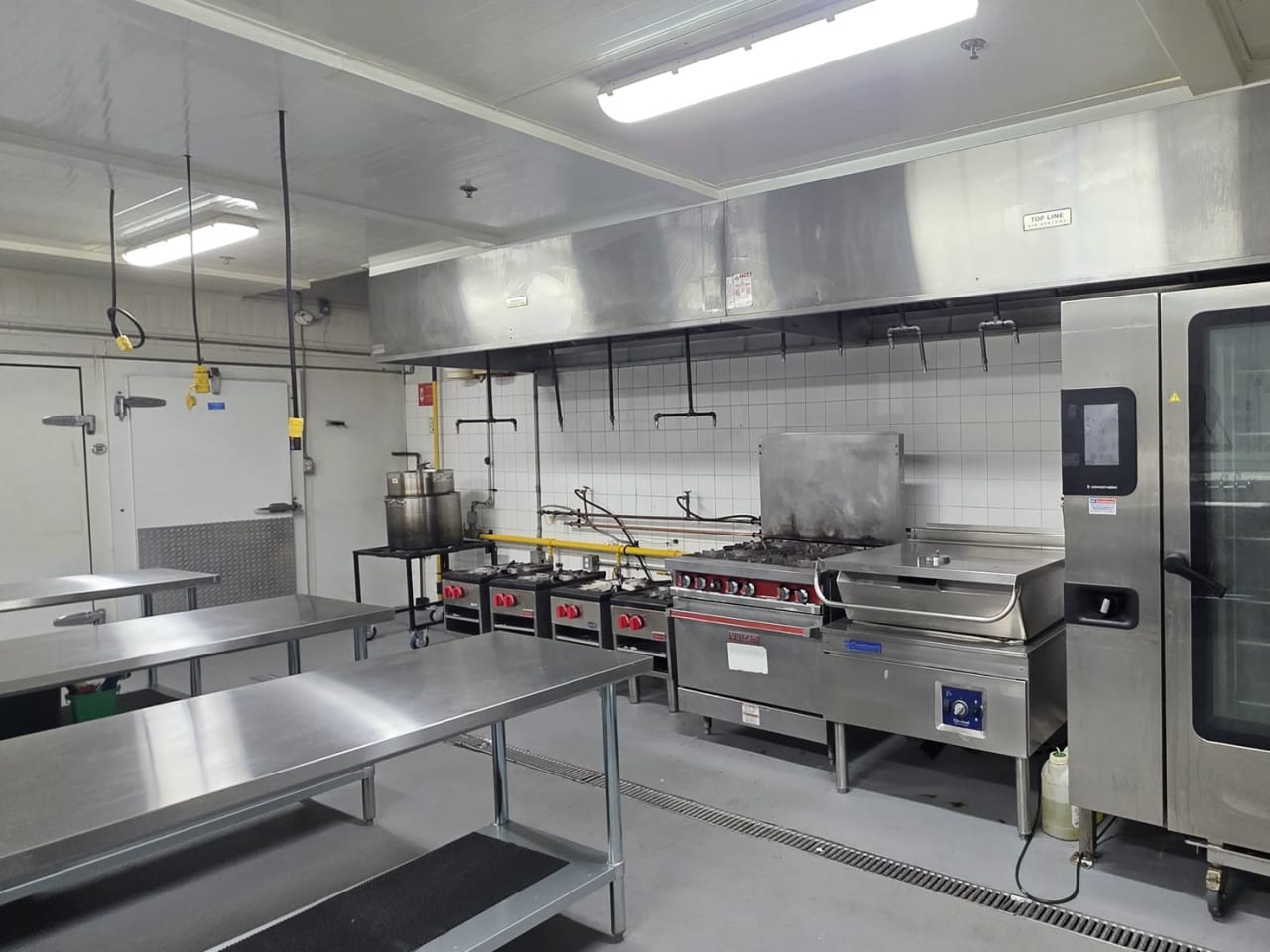 MiFoodStudio commercial cook line in Mississauga, six-burner range and stock pot burners beside a full-size combi oven, under a 20-foot stainless exhaust hood