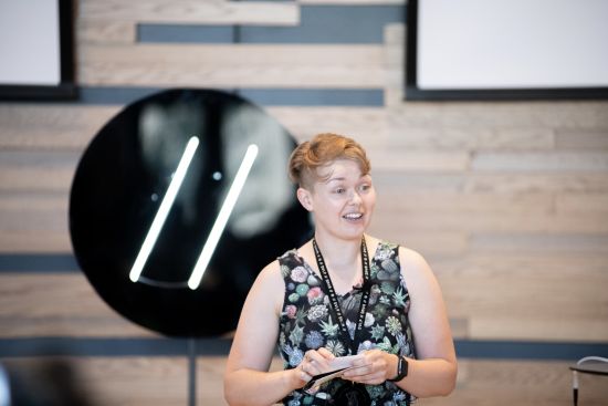 Kim Schlesinger talking to a conference audience in front of the Develop Denver logo.