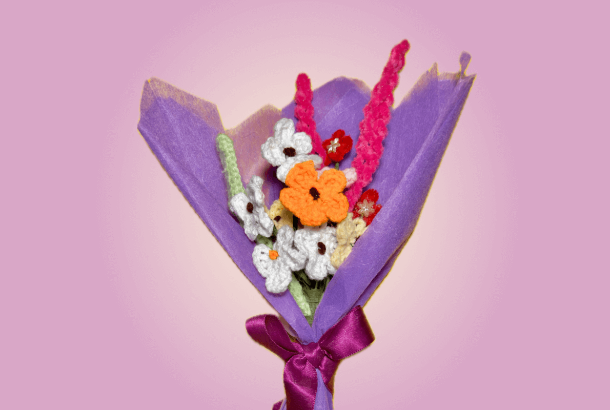 Handmade mini crochet bouquet wrapped in elegant purple paper with a satin ribbon, featuring delicate knitted flowers in white, orange, and pink, perfect for gifting and special occasions.
