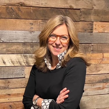 Karen Dunphey smiling and posing for photo infront of a wooden backdrop.
