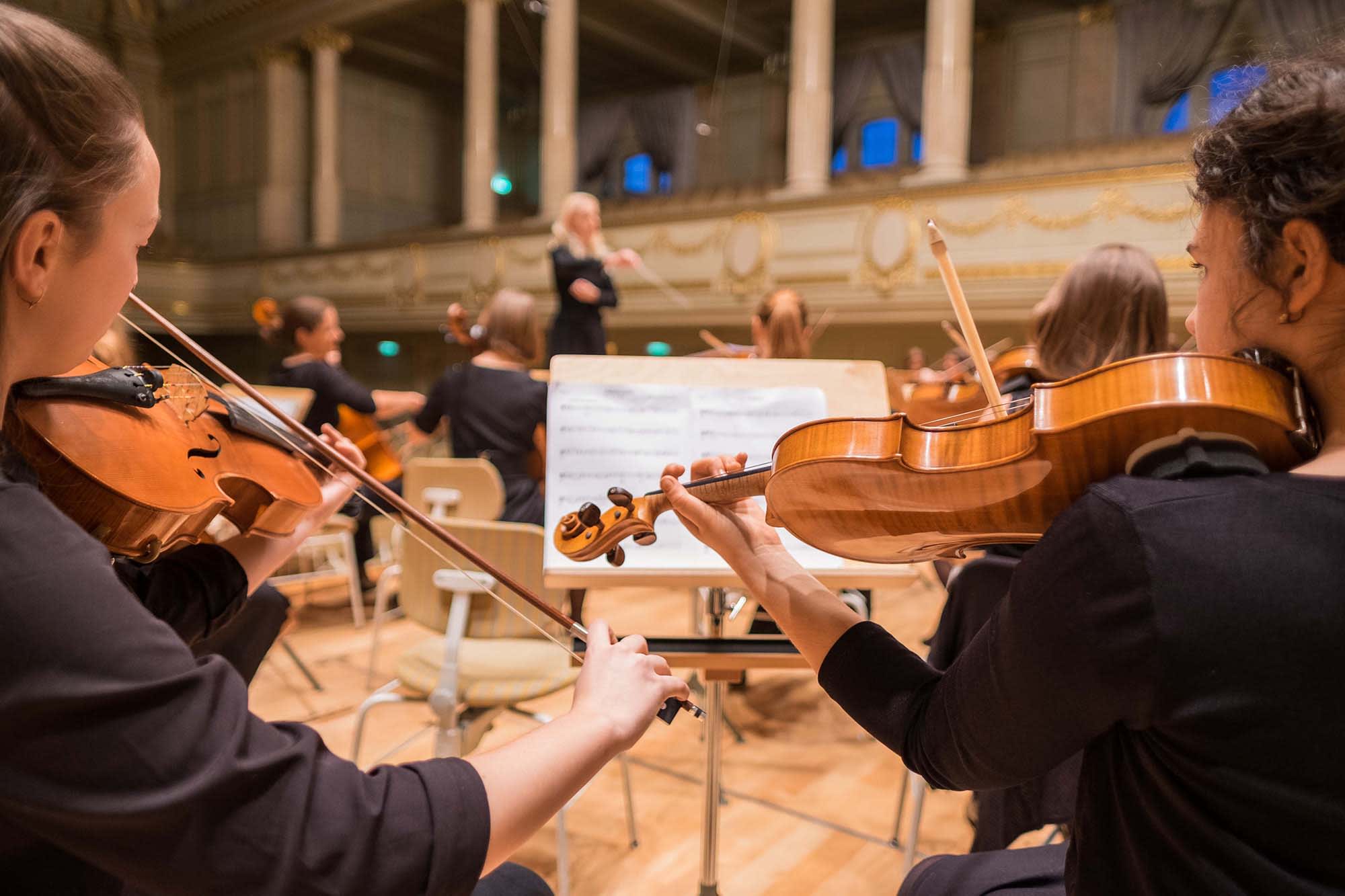 orchestra performing with conductor using sheet music with aritae students performing