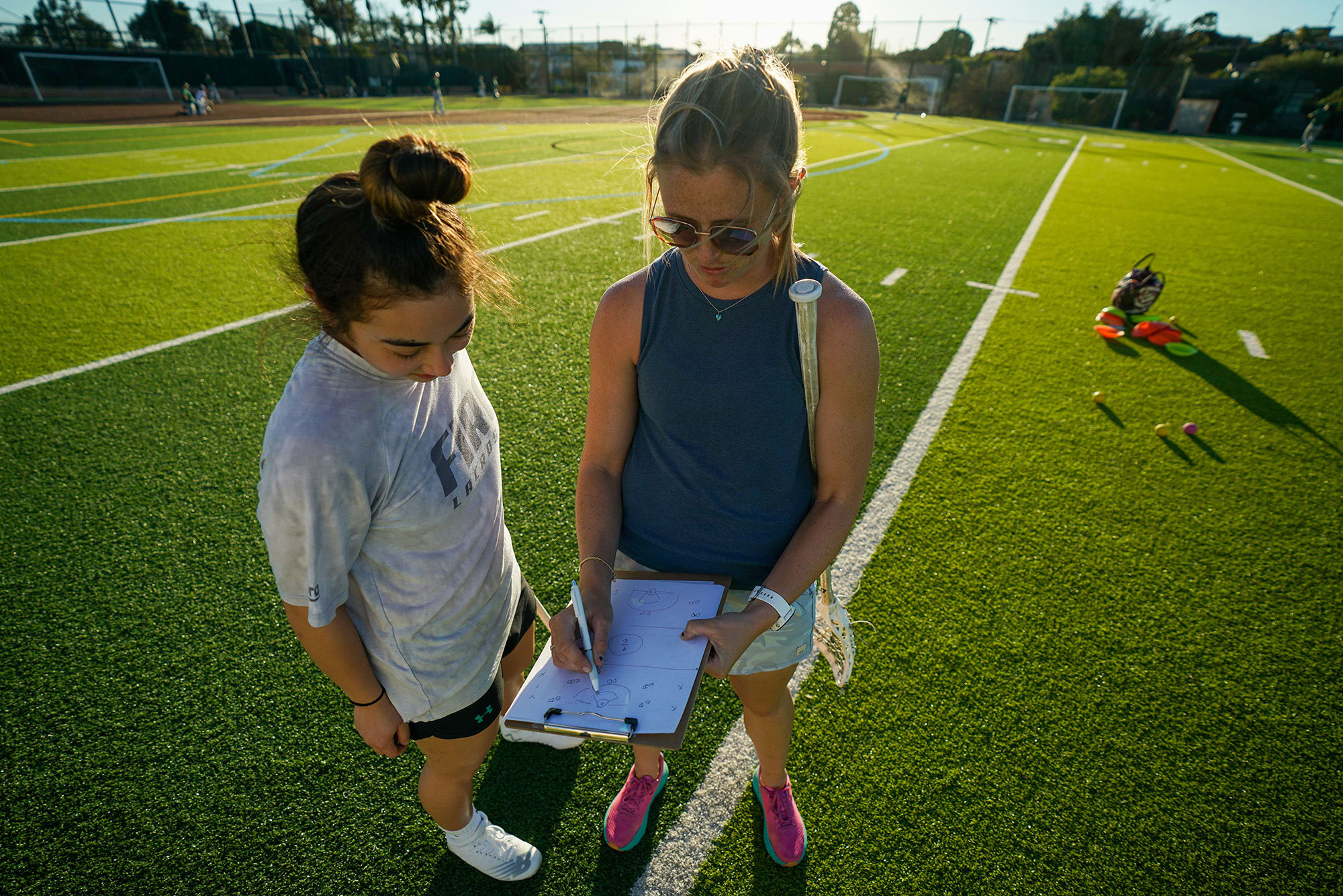 coach showing young woman a play on a clipboard in a green field