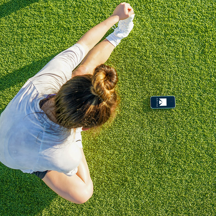 young woman stretches on a field with phone on ground showing ARITAE mobile app