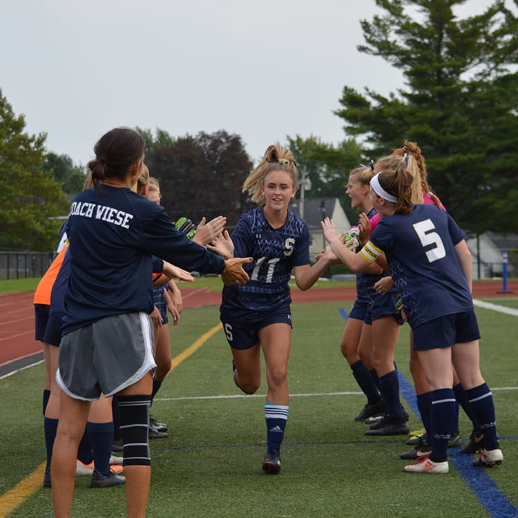 girl running through her team giving high-fives on a field