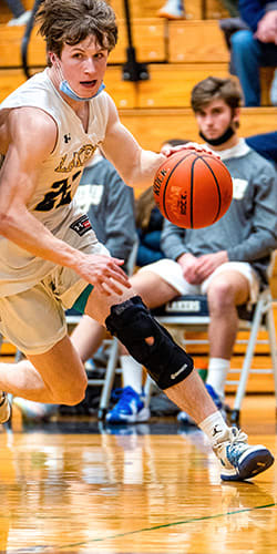 young man runs on basketball court with ball, while another watches from the sidelines
