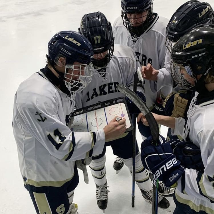 hockey coach shows players a plan on a small whiteboard in the rink