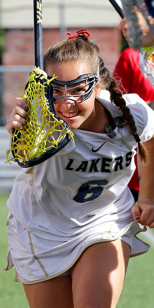young girl playing lacrosse and running down field with support of her teamates.