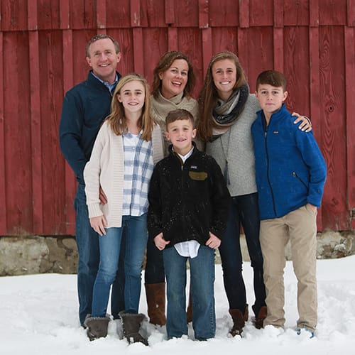 ARITAE CEO and Chief Inspirational Officer Jerry Morrissey and his family in front of their barn in the snow taking a smiling family photo.
