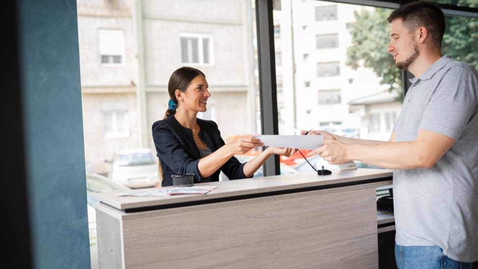 Front desk employee hands in a visitor sign in sheet to a visitor