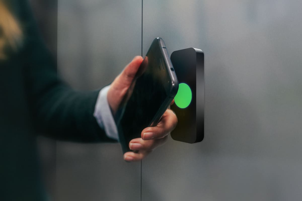 An image of a person tapping their phone to a Kisi access control reader to unlock a door