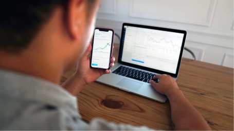 An image of a man following the stock market on mobile and laptop