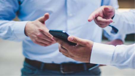 A picture of a man showing something on his mobile phone to another man