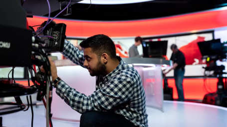 An image of a tv studio showing different men working on setting up cameras
