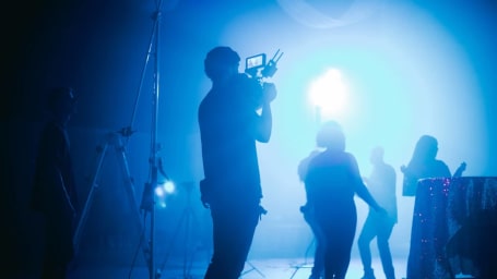 An image showing people working on a set with the focus on the man operating the video camera