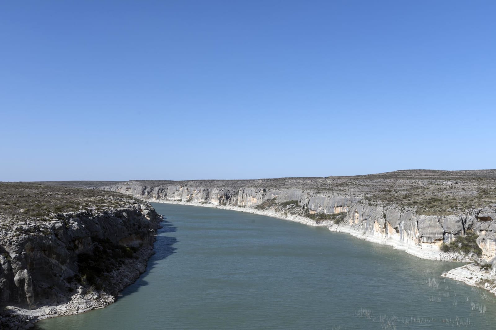 A green-blue river curves between pale limestone cliffs under a cloudless sky in Amistad National Recreation Area near Del Rio, Texas.