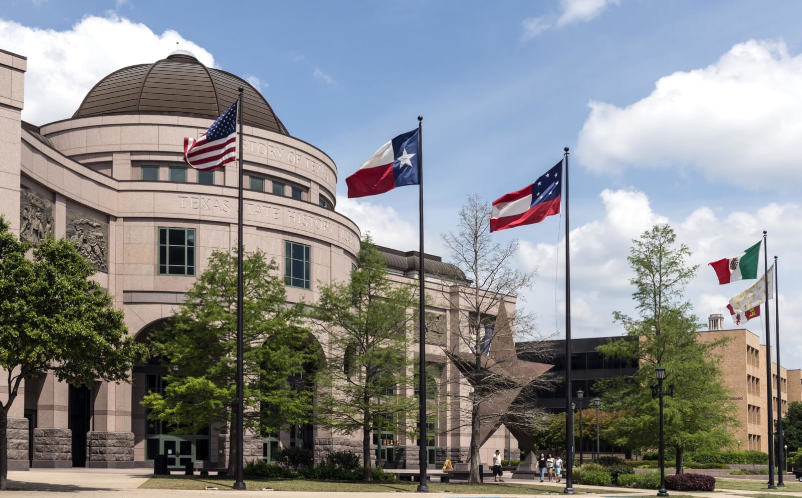 The pink stone rotunda and flagpoles of the Bullock Texas State History Museum in Austin, with flags of Texas and the nation.