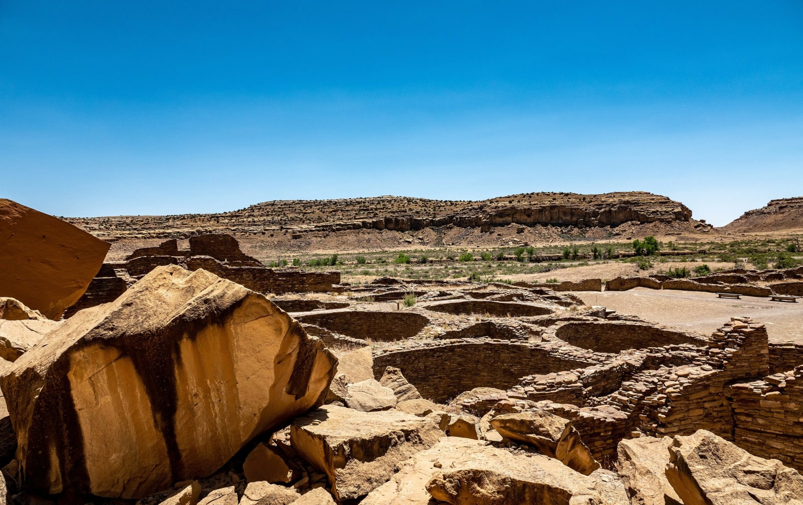 The walled rooms of Pueblo Bonito seen from above, a fallen sandstone block in the foreground and the canyon rim beyond